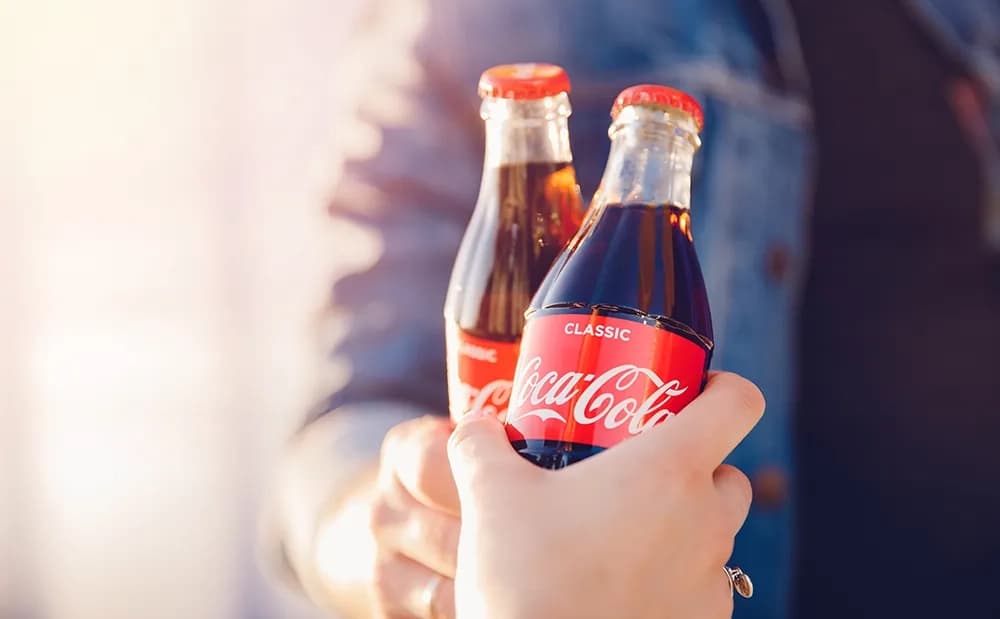 Hand holding out two classic Coca-Cola glass contour bottles in warm sunlight