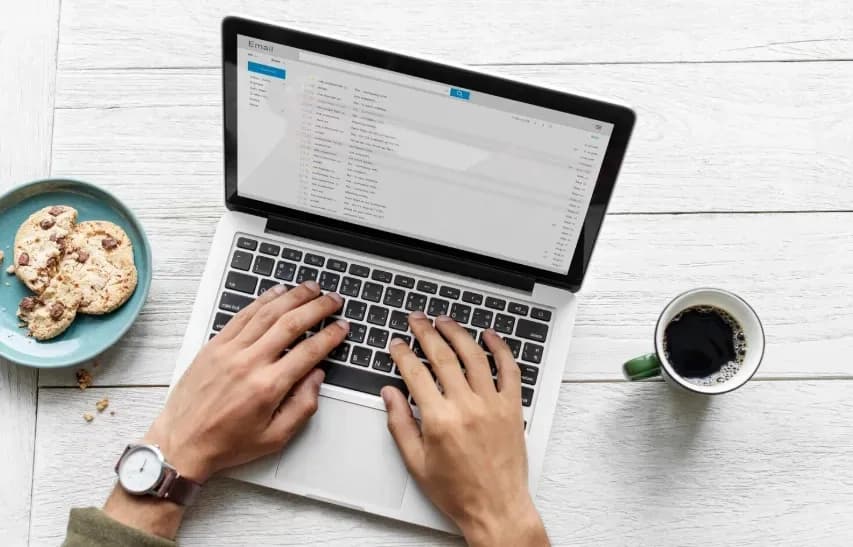 Person at a laptop working through an email inbox, with coffee and cookies beside them