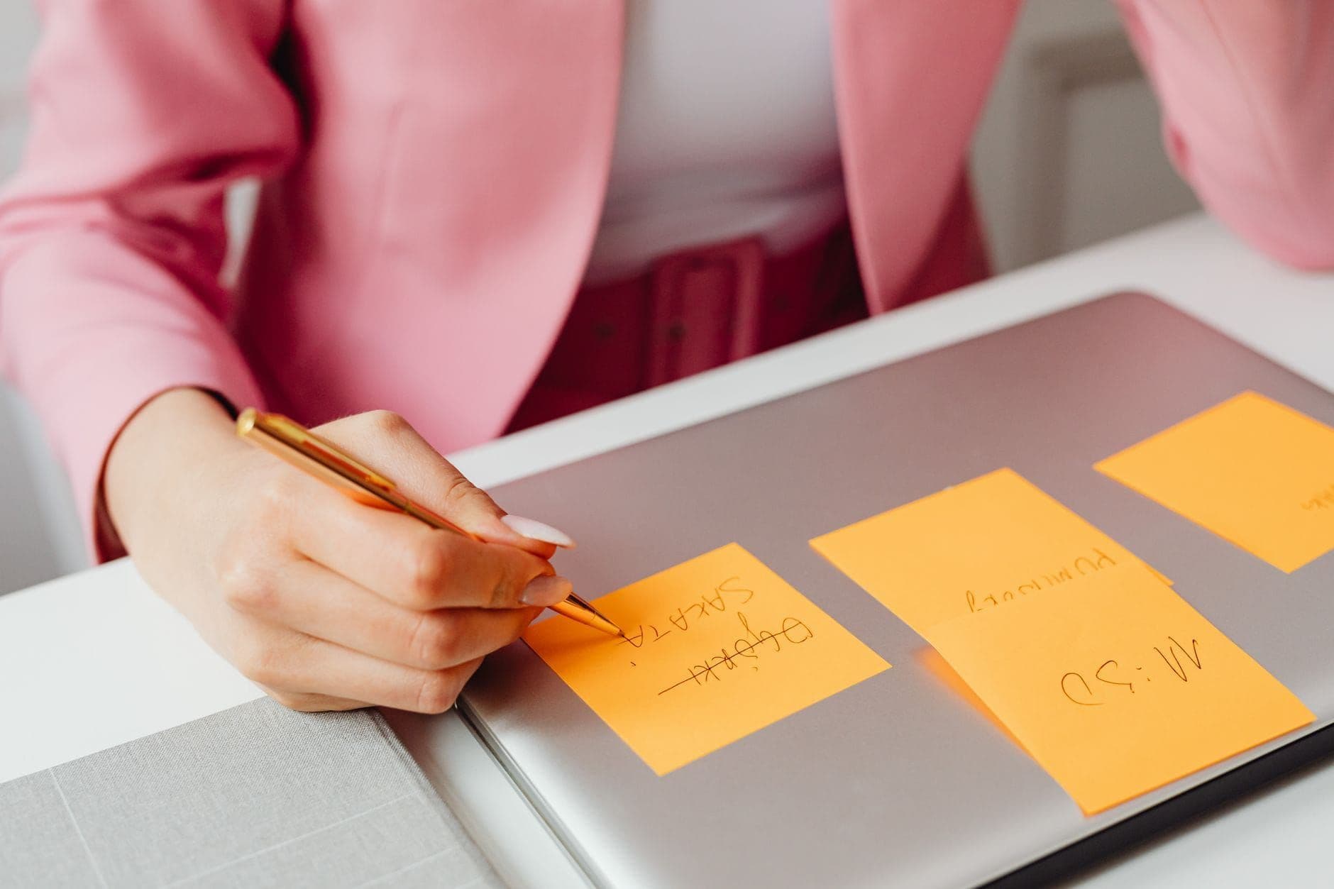 Person writing on sticky notes while planning on a laptop