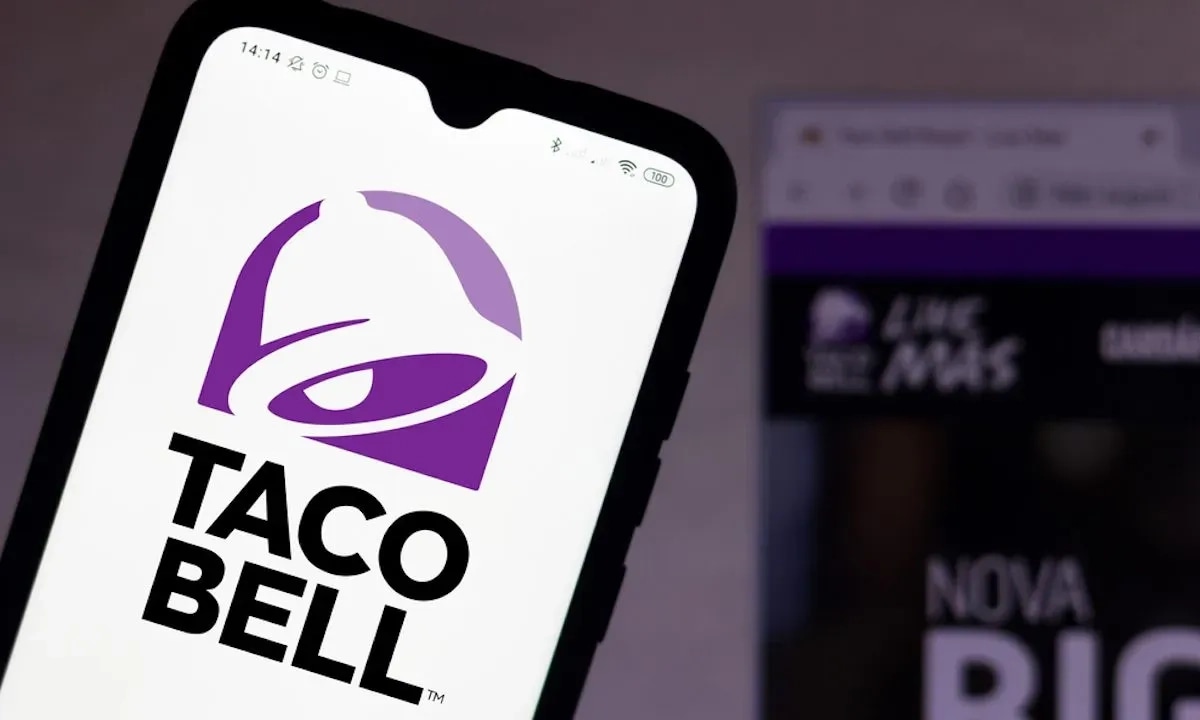 Taco Bell logo on a phone screen with the brand's website blurred in the background