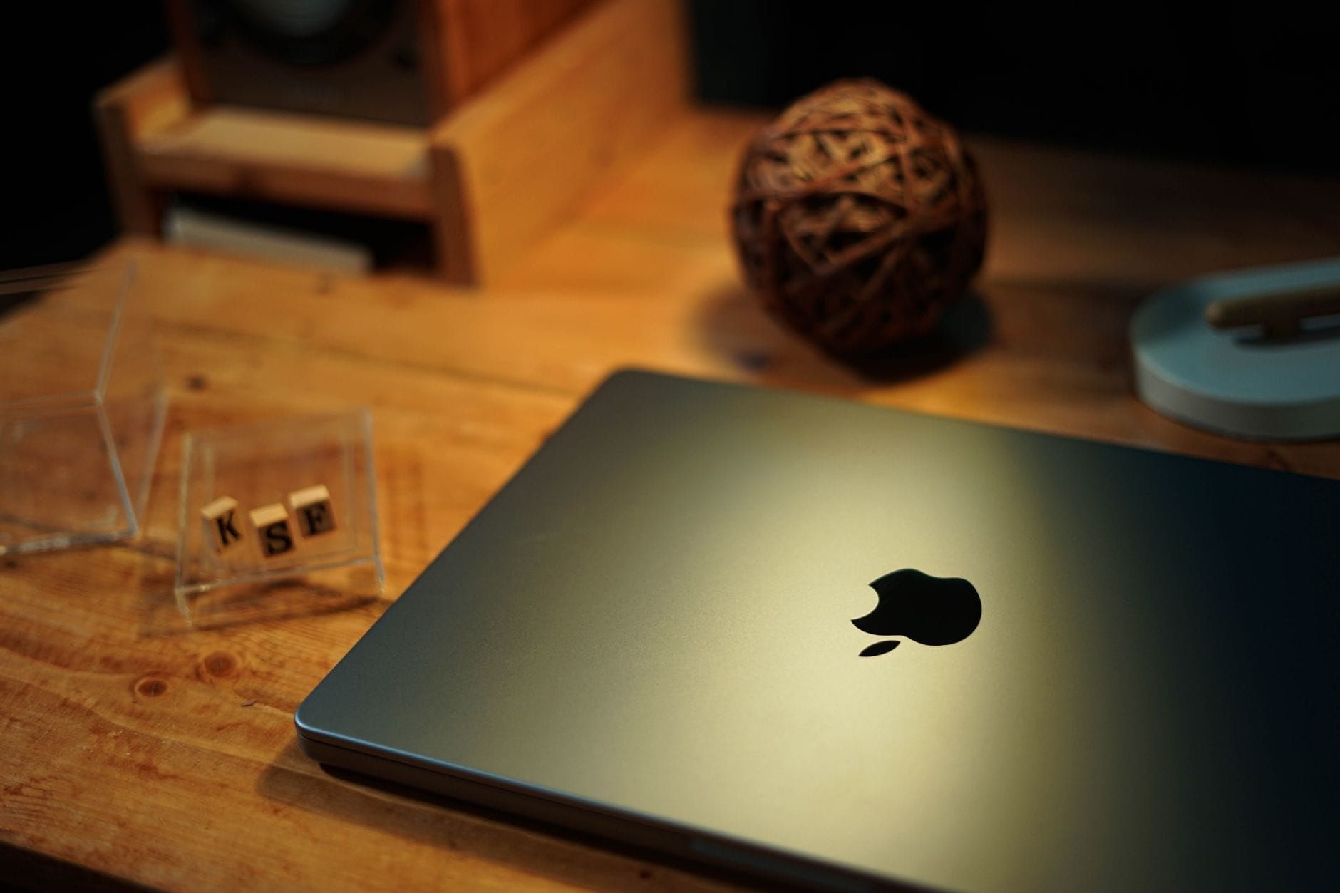 MacBook with the Apple logo resting on a wooden desk under warm light
