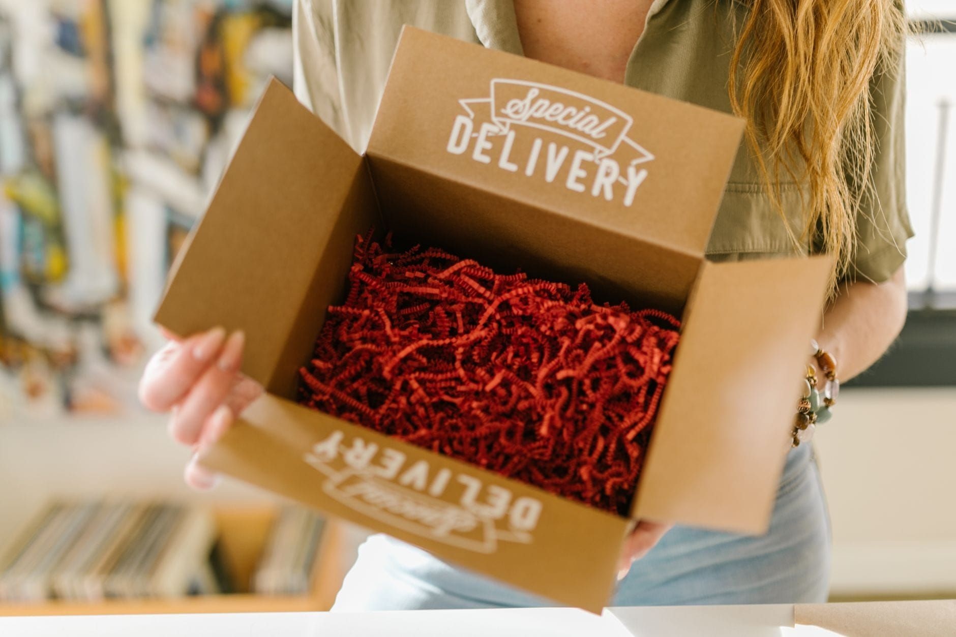 Customer opening a branded delivery box filled with red crinkle paper