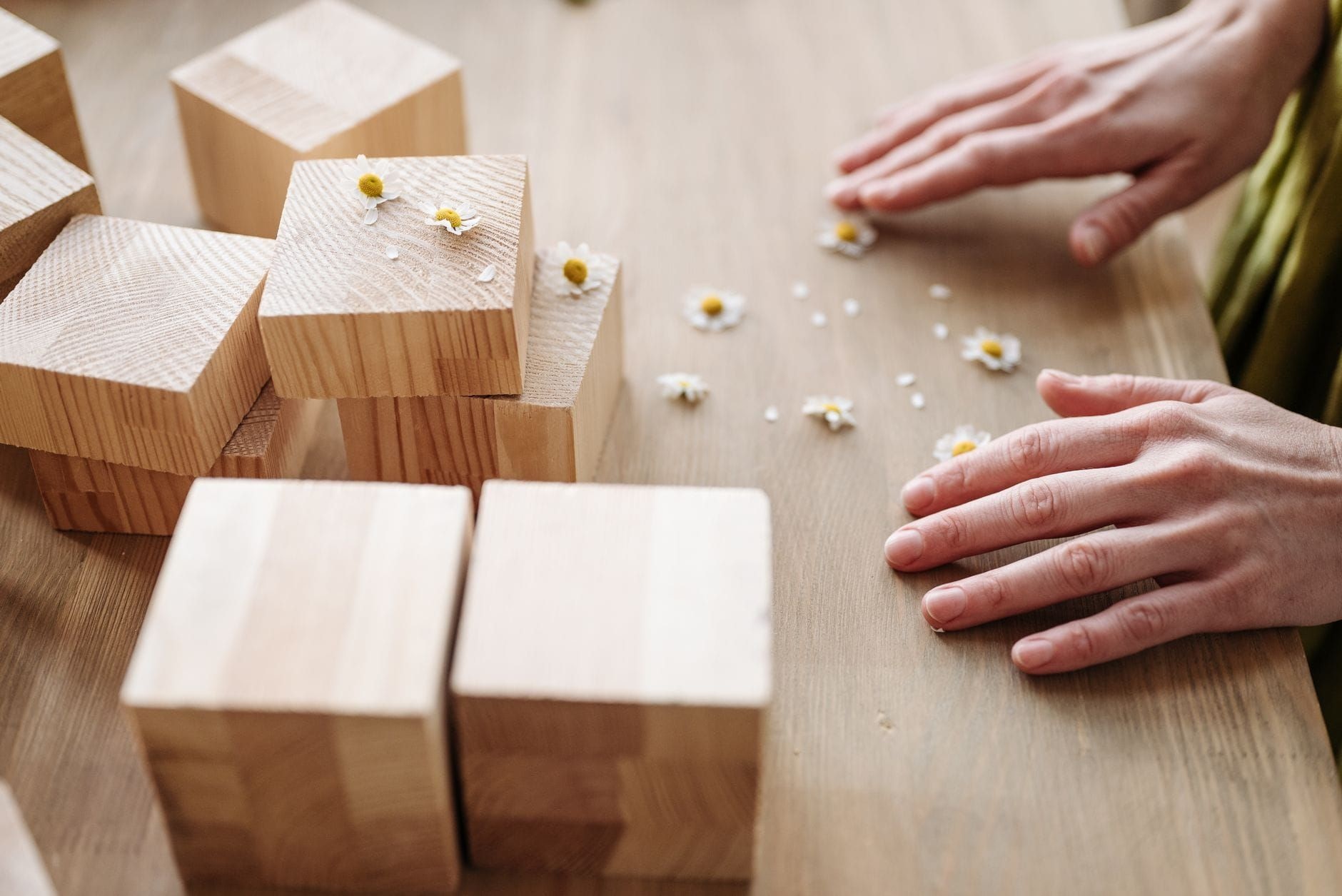 Hands arranging wooden blocks into a structure on a light surface