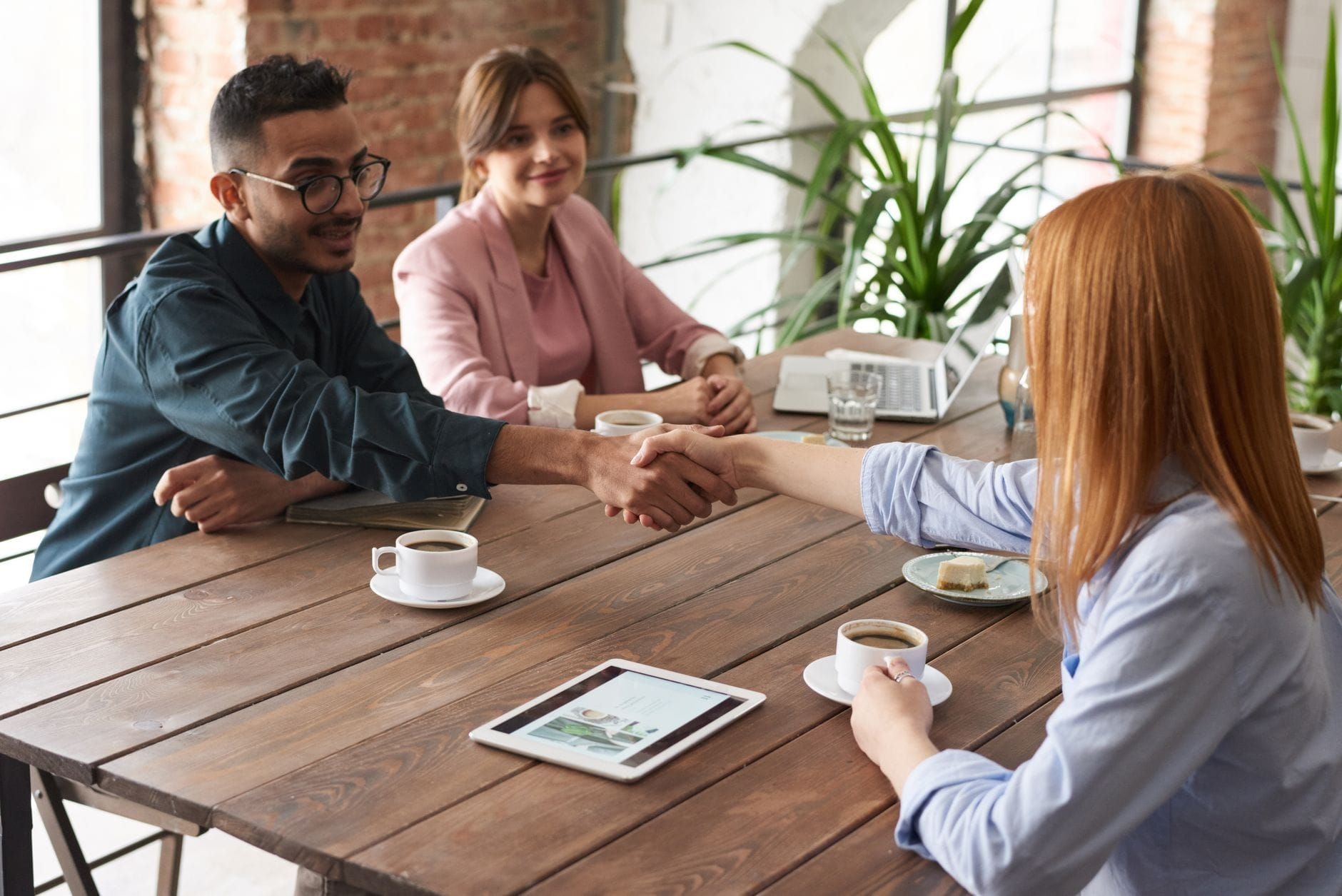 Colleagues shaking hands over coffee at a wooden meeting table