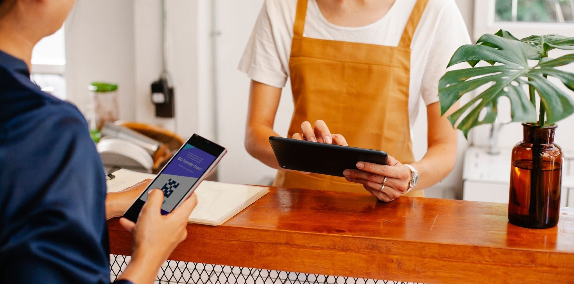 Cafe employee using a tablet while a customer pays with their phone at the counter