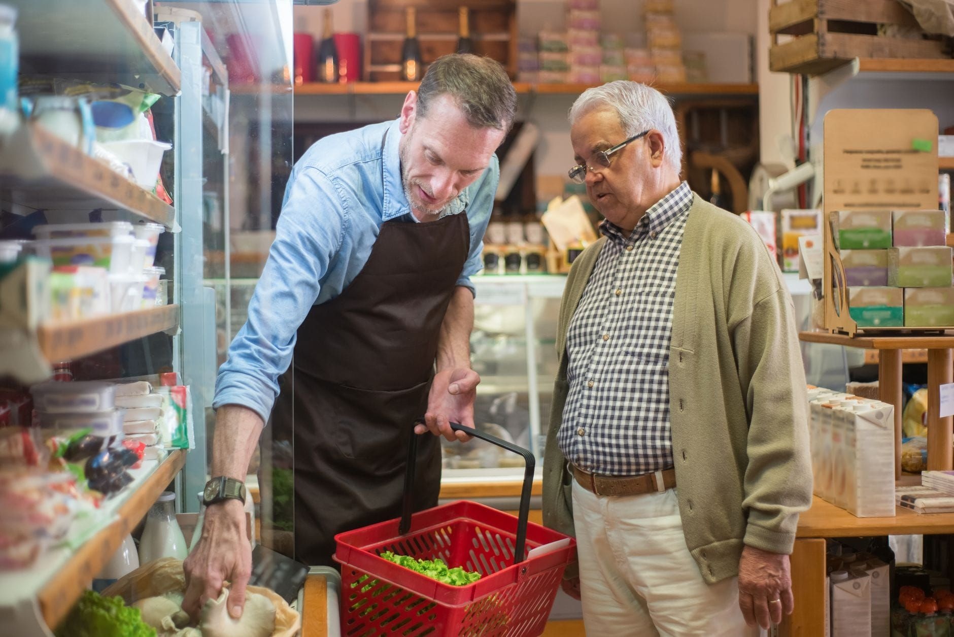 Shop assistant helping an older customer choose groceries