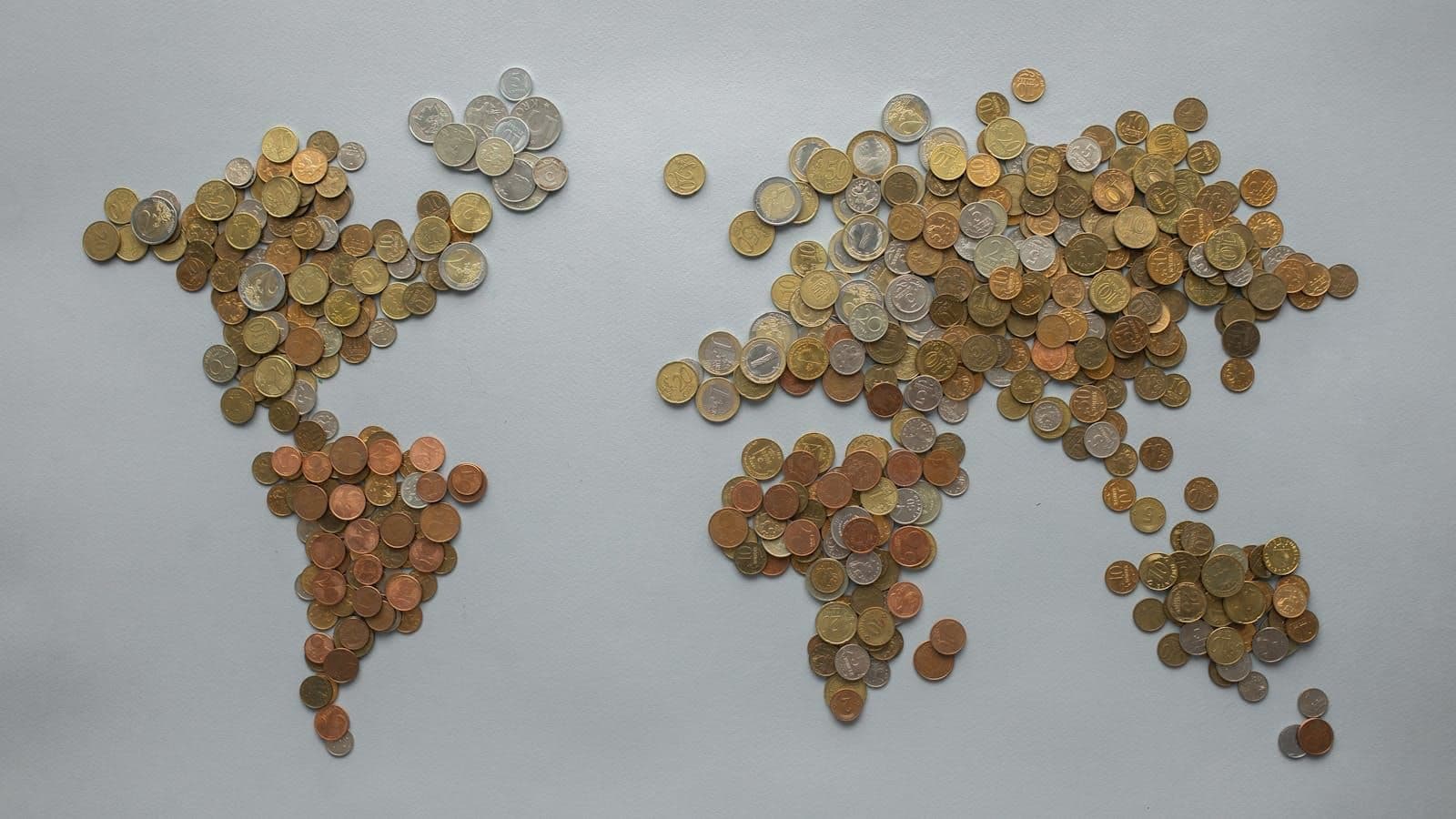 World map formed from piles of assorted coins on a plain grey surface