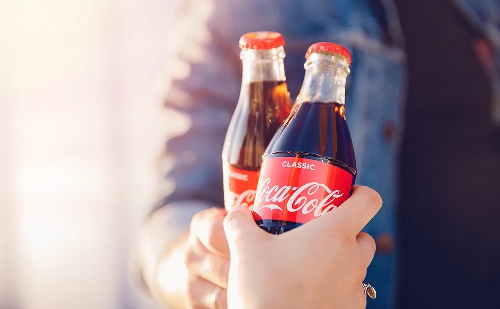 Hand holding out two classic Coca-Cola glass contour bottles in warm sunlight