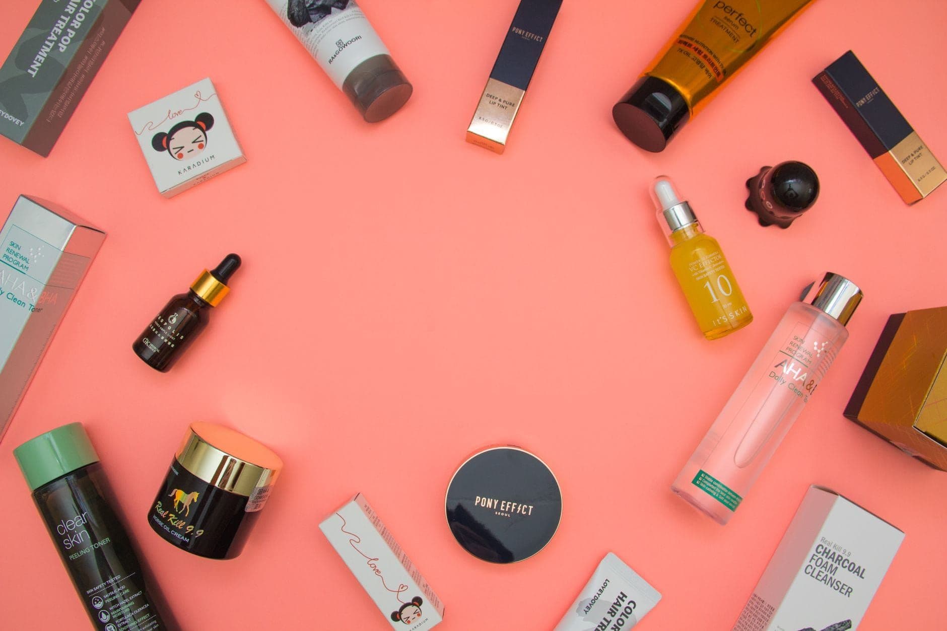 Flat lay of assorted beauty products from different brands on a pink background