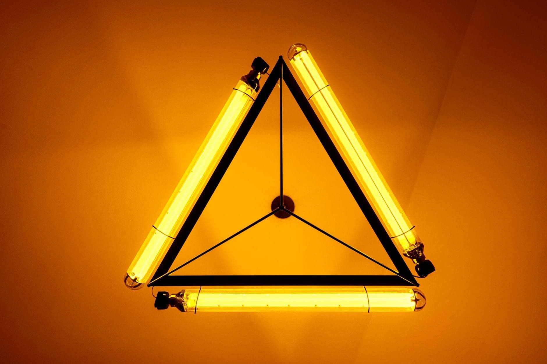 Triangular neon lamp glowing amber against an orange background