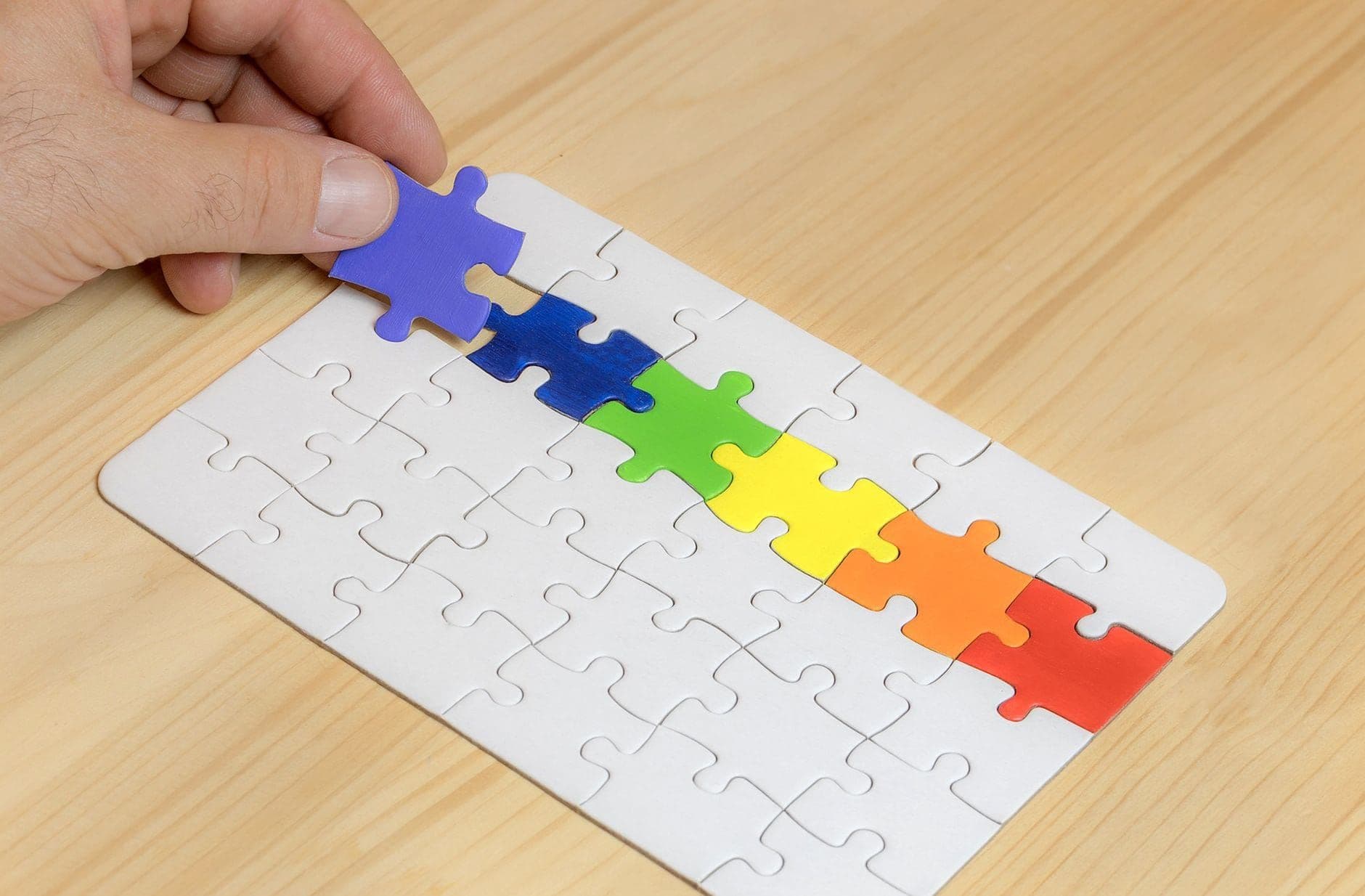 Hand placing the final piece into a row of colorful puzzle pieces