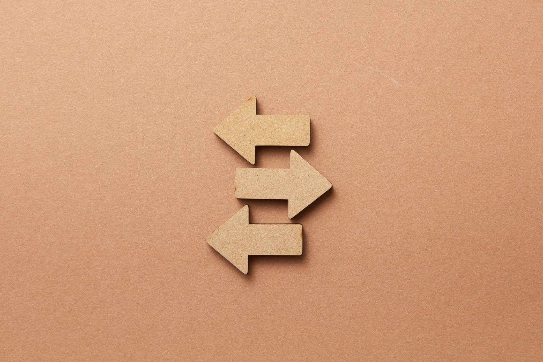 Three wooden arrows pointing in different directions on a beige background