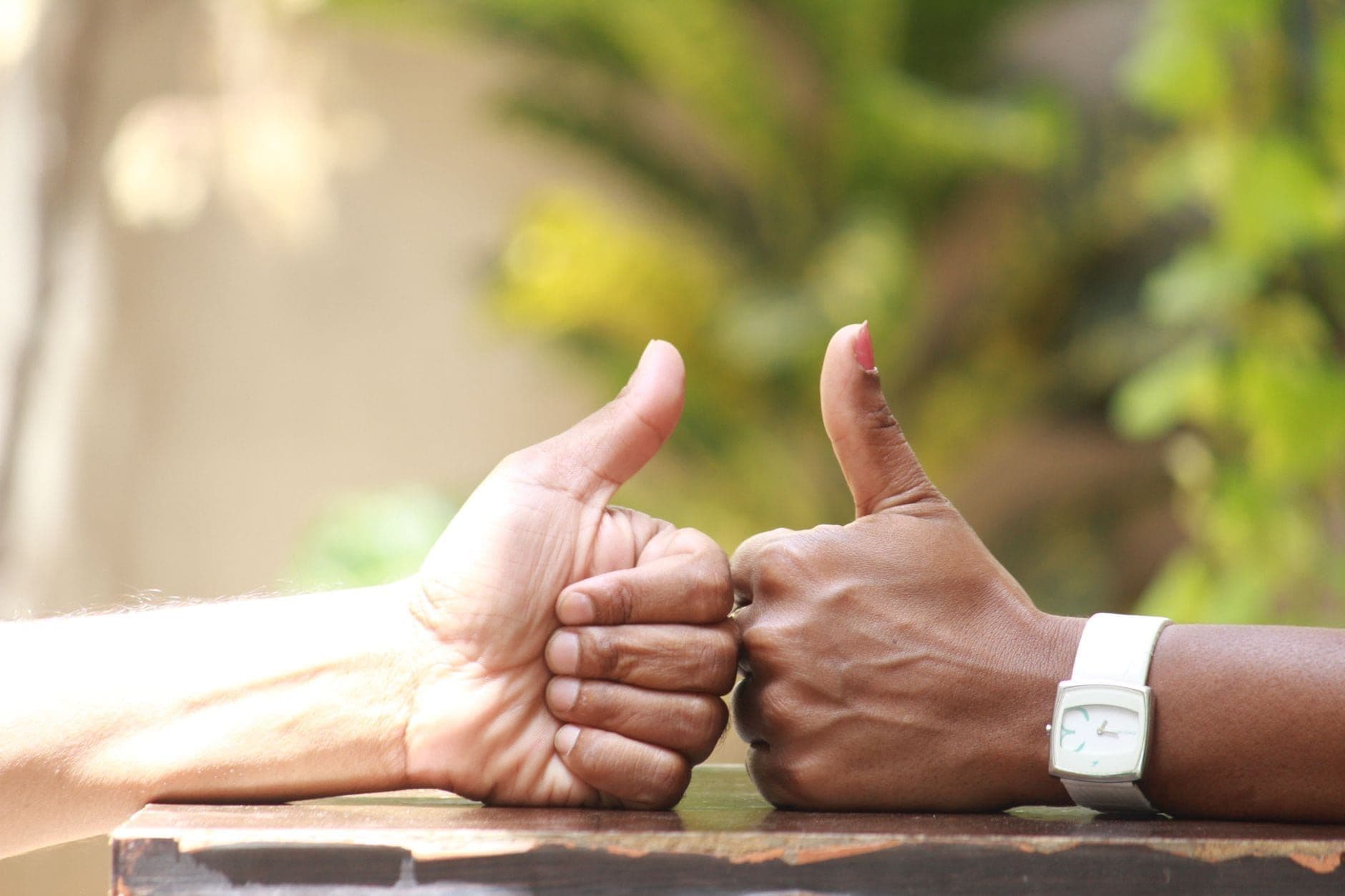 Two people giving a thumbs up outdoors in warm sunlight