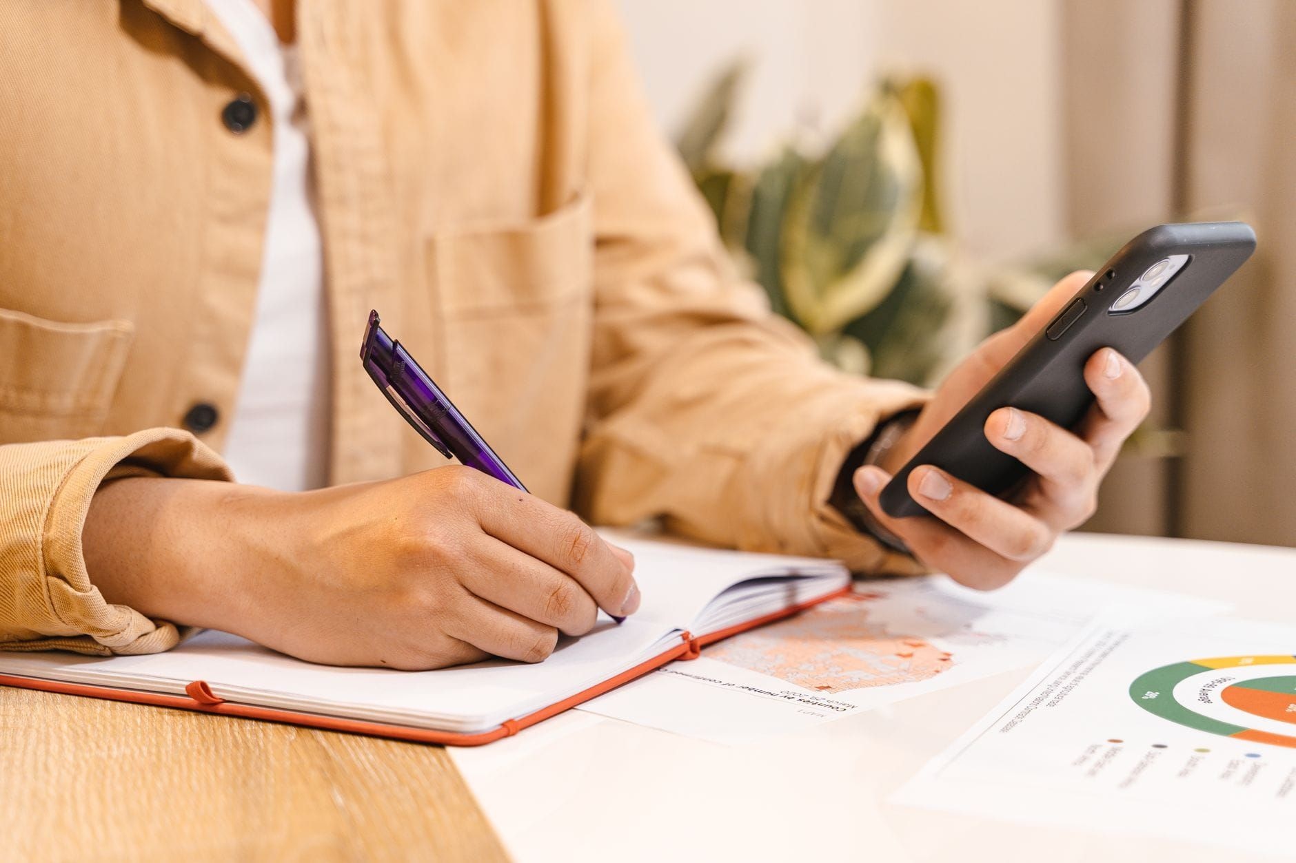 Hands holding a smartphone while taking notes beside a printed chart