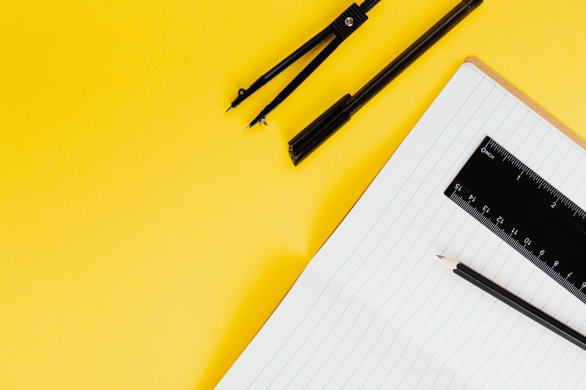 Notebook with a pencil, ruler and compass arranged on a yellow surface