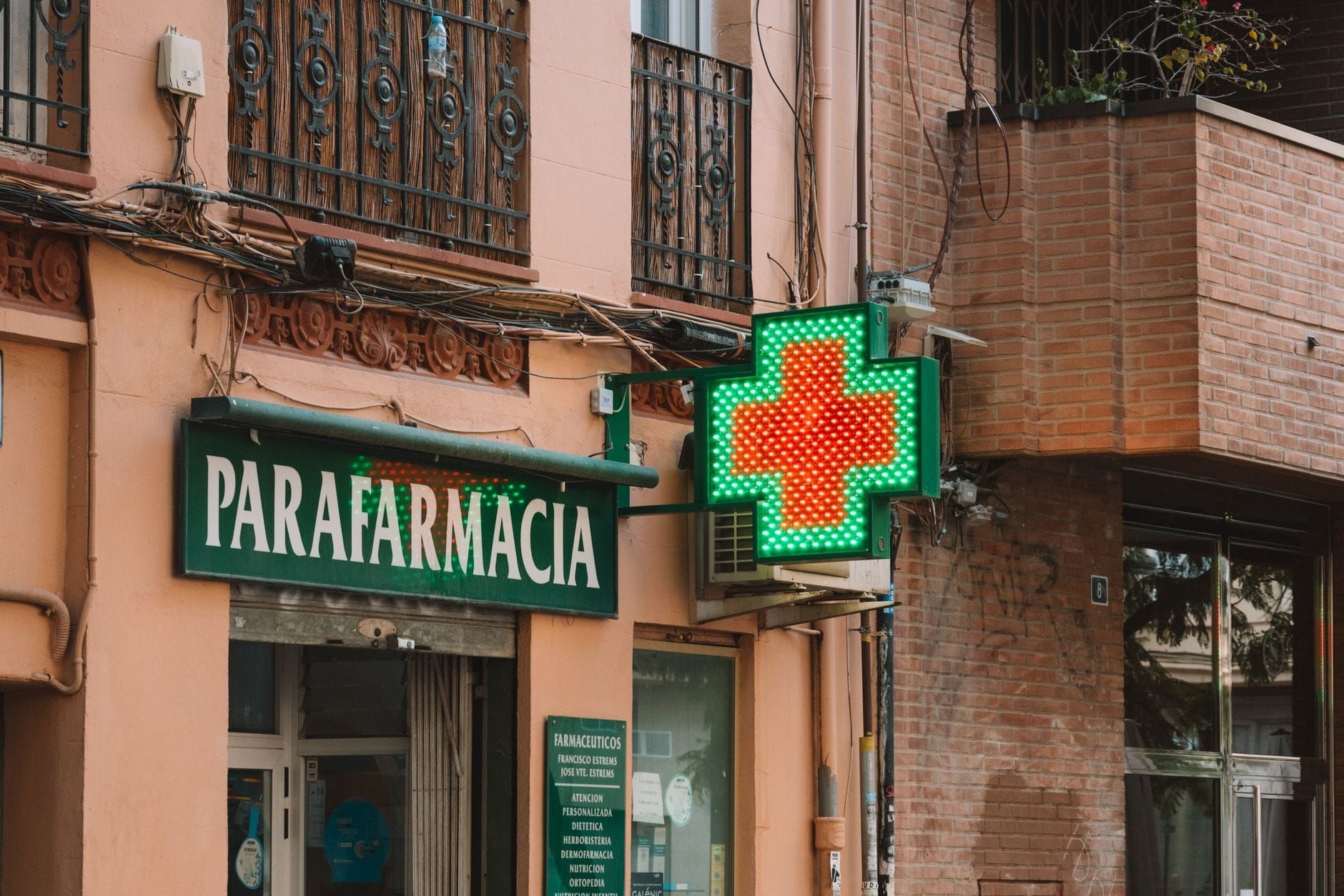Green neon cross sign above a pharmacy storefront